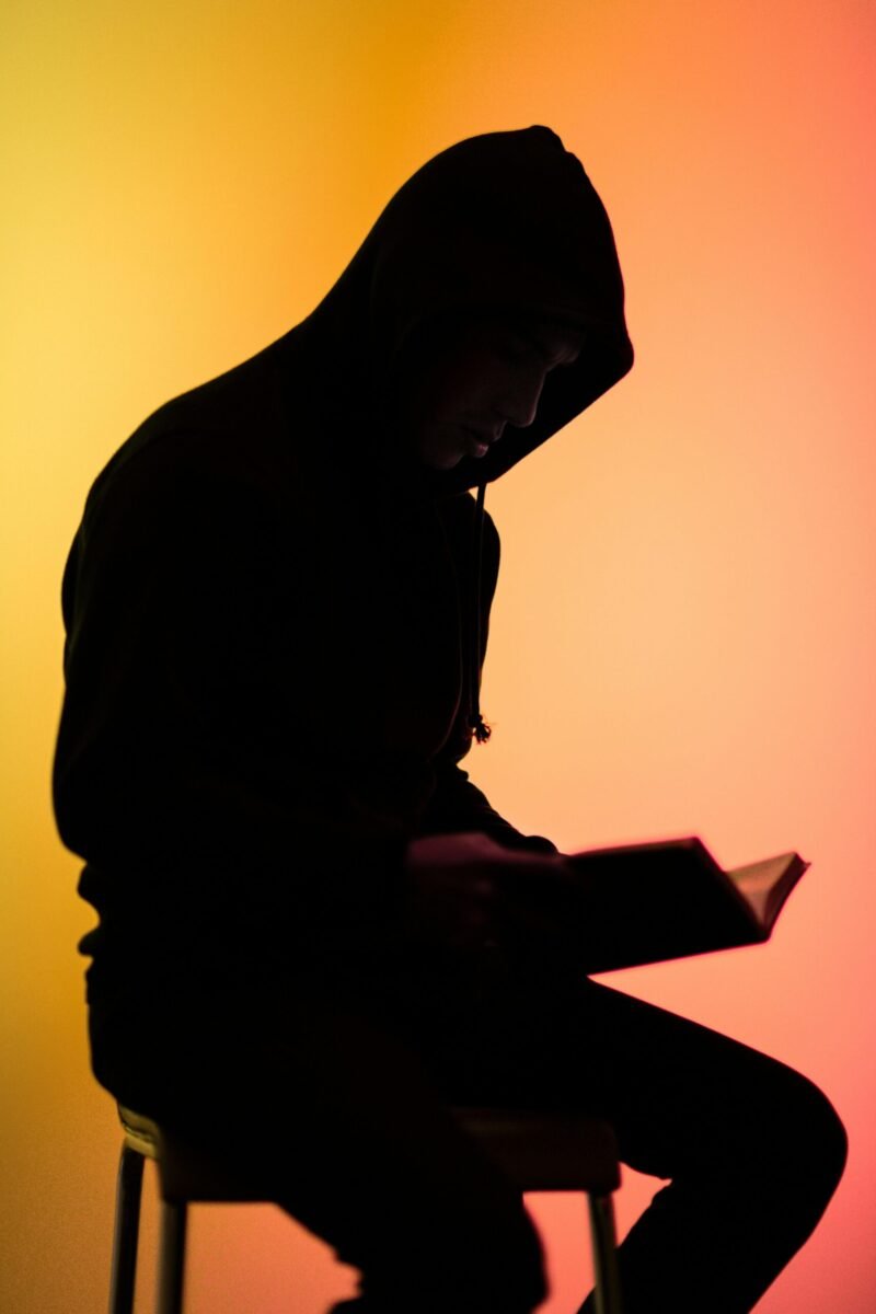Silhouette of a man reading a book with a colorful gradient background.